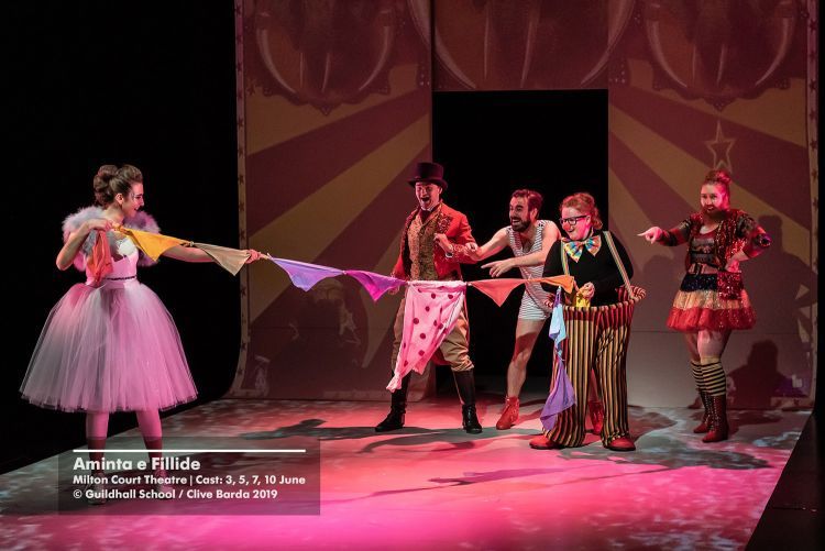 Actors in circus costumes holding bunting on the set of an opera